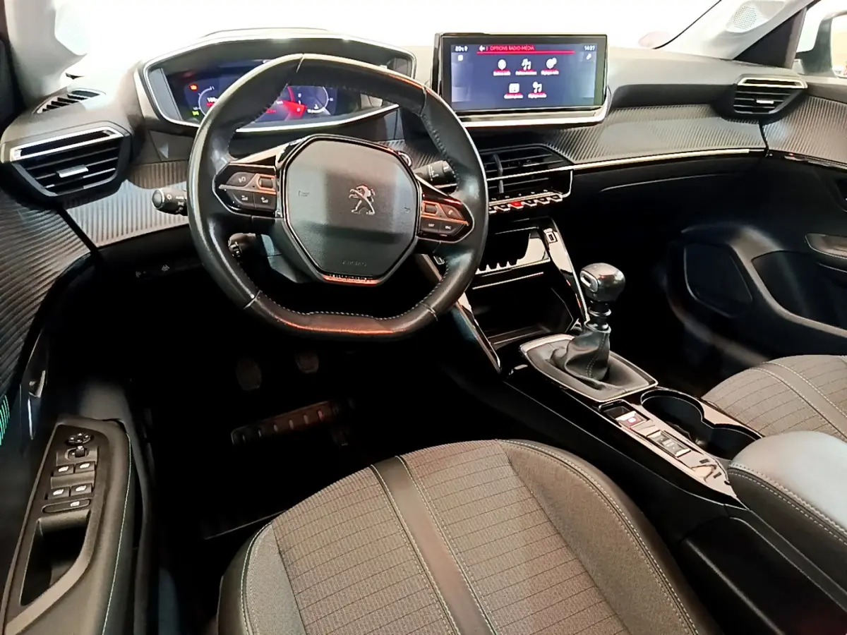 Vue intérieure avant de la Peugeot 208 PureTech 100 avec volant cuir, écran tactile et levier de vitesse manuel.