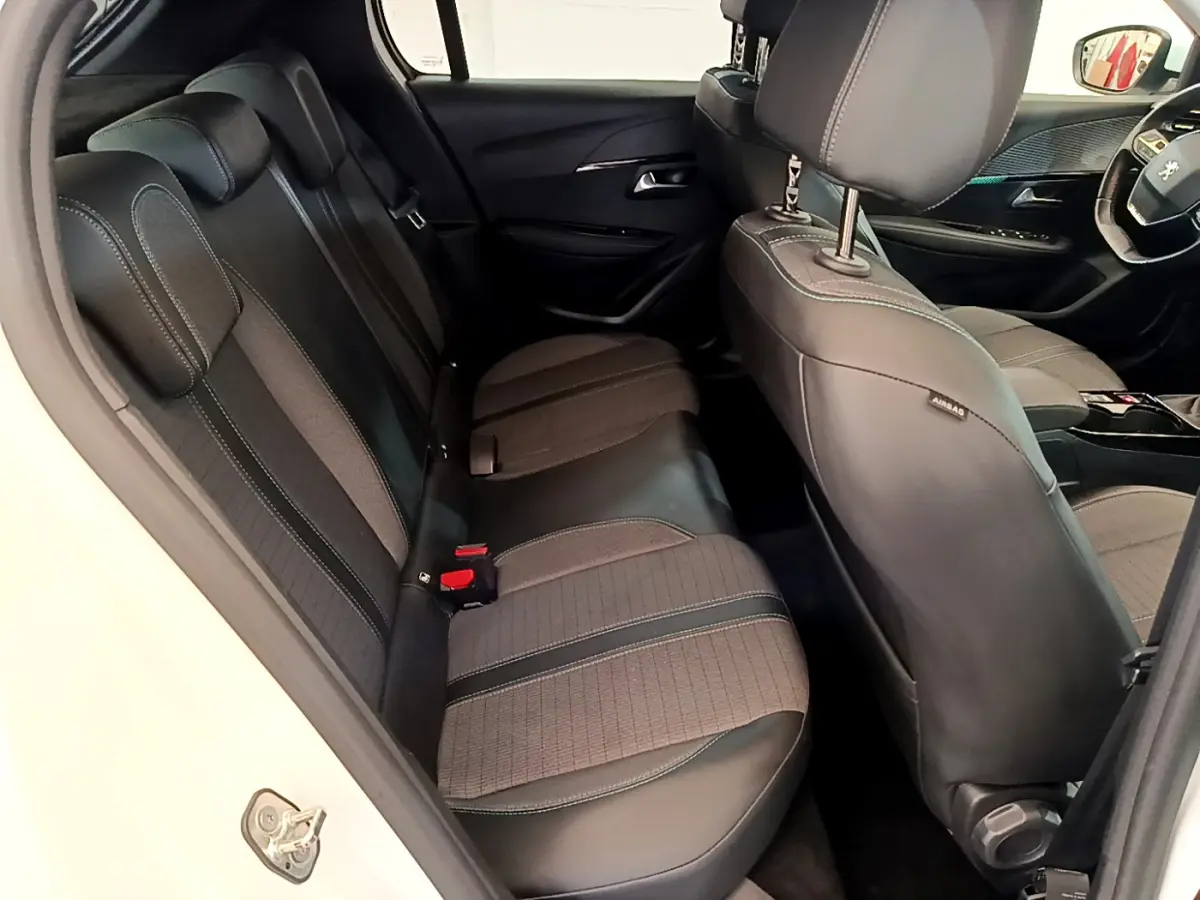 Intérieur arrière de la Peugeot 208 blanc, vue côté gauche montrant les sièges en tissu et cuir avec surpiqûres contrastées.