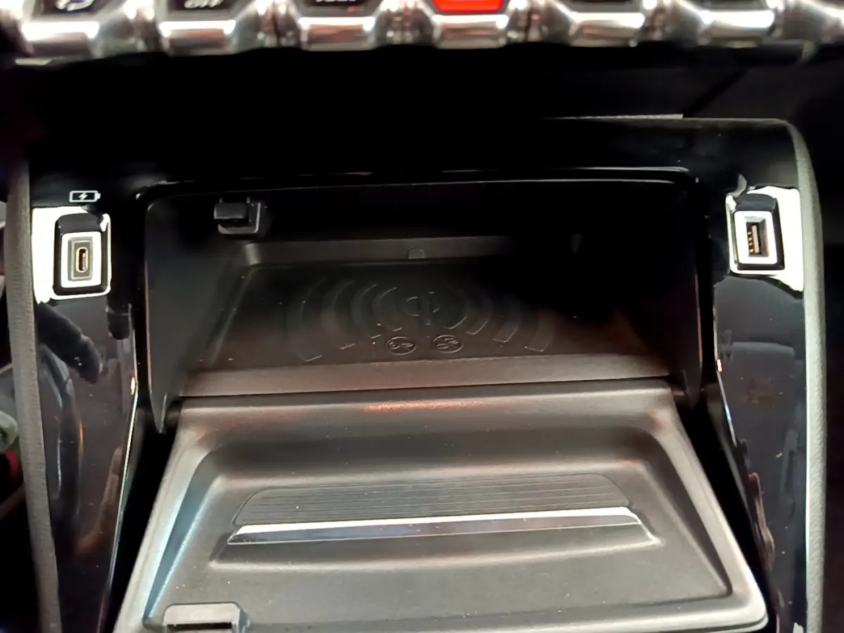 Zone de recharge par induction et ports USB intégrés dans la console centrale noire d'une Peugeot 208 blanche.