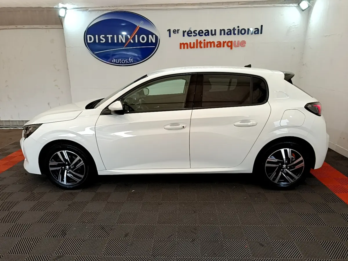 Profil côté gauche d'une Peugeot 208 blanche PureTech 100 S&S Allure Business de 2020 en intérieur showroom.