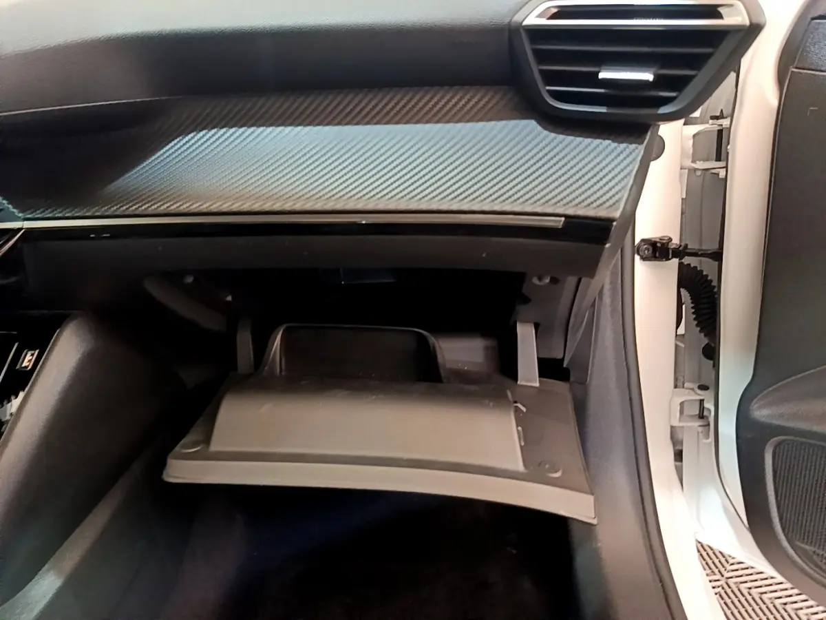 Vue intérieure côté passager du Peugeot 208 blanc 2020, boîte à gants ouverte sous tableau de bord noir avec insert carbone.