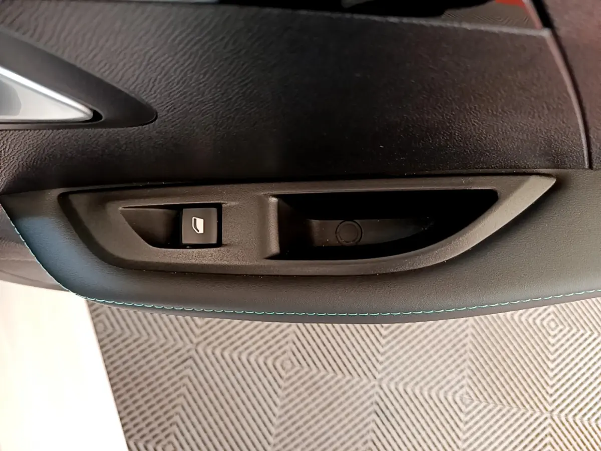 Gros plan sur la poignée intérieure et bouton de lève-vitre côté gauche d'une Peugeot 208 blanche, finition Allure Business.