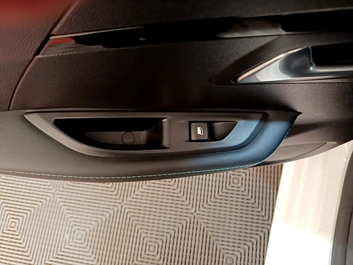 Gros plan sur la poignée intérieure côté gauche de la porte noire de la Peugeot 208 blanche, bouton de verrouillage visible.