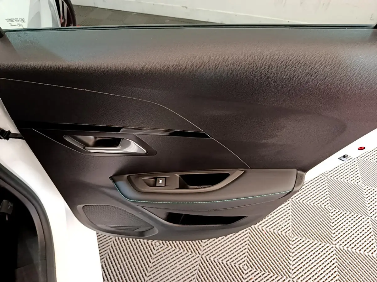 Vue rapprochée de la porte intérieure côté gauche noire avec surpiqûres bleues d'une Peugeot 208 blanche 2020.