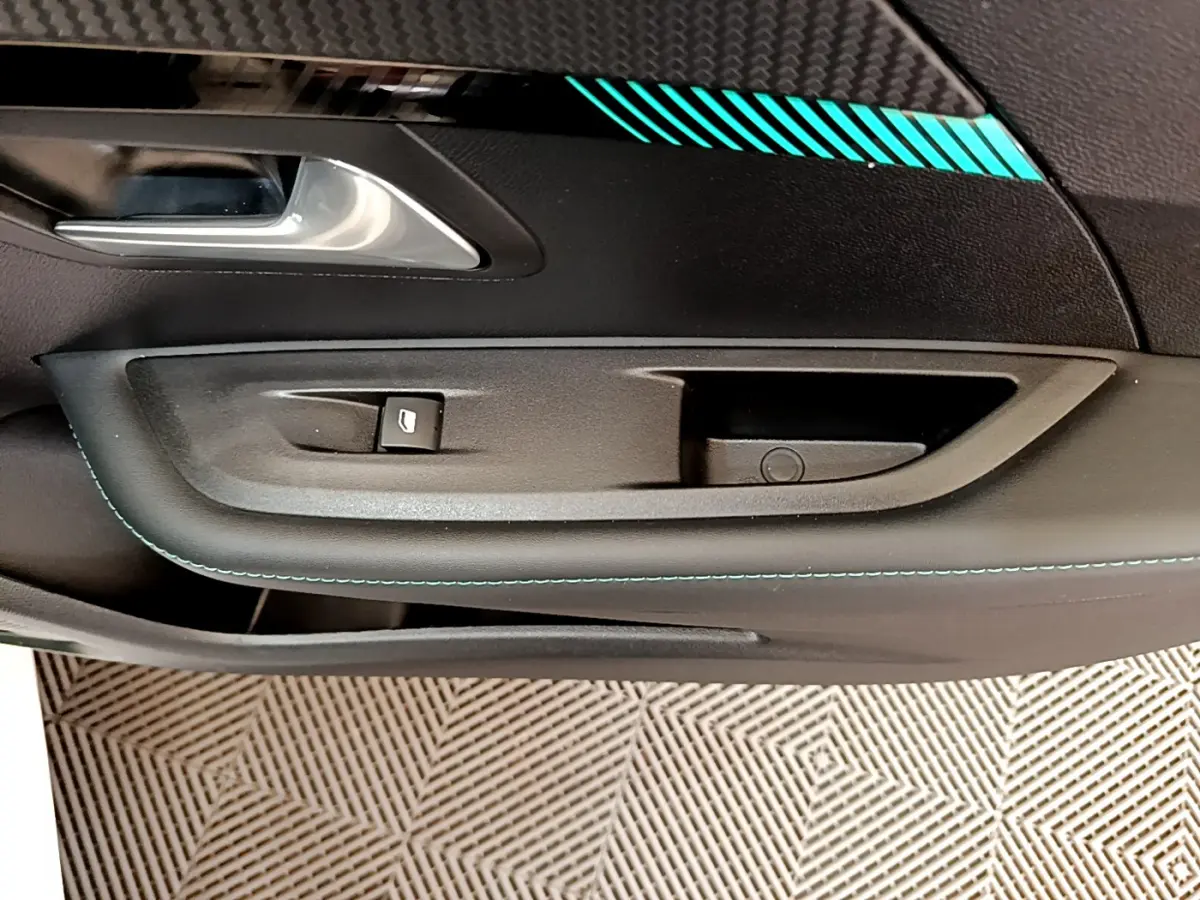 Gros plan sur la poignée intérieure côté conducteur de la Peugeot 208 blanche avec surpiqûres bleues et insert carbone.