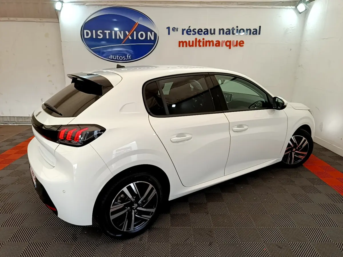 Peugeot 208 blanc vue 3/4 arrière droit en intérieur, feux arrière LED et jantes alliage distinctives visibles.