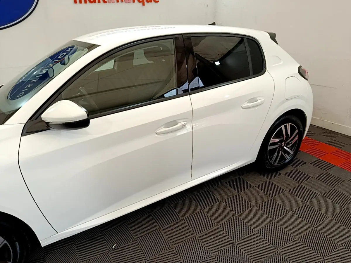 Profil côté gauche de la Peugeot 208 blanche de 2020, avec jantes alliage et vitres teintées dans un showroom.