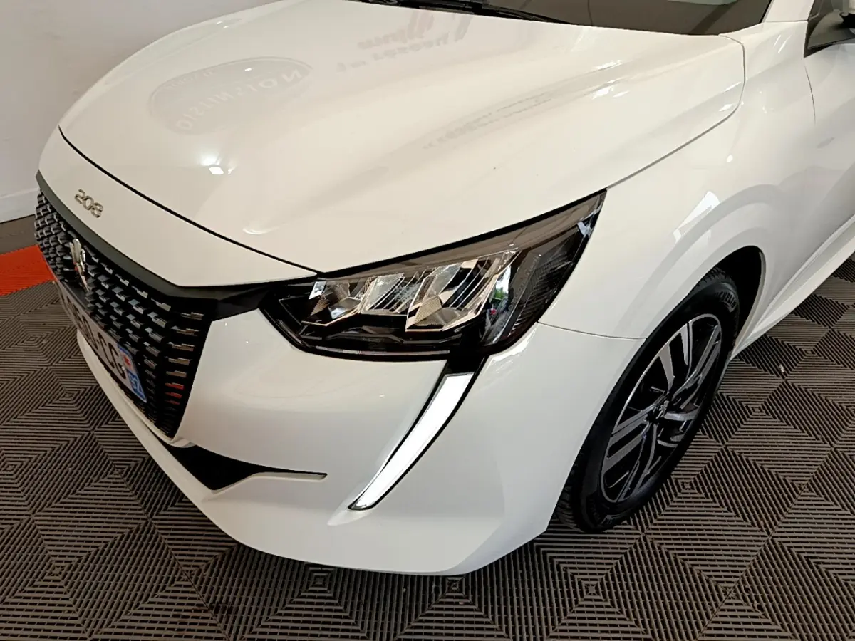 Vue 3/4 avant droit d'une Peugeot 208 blanche mettant en valeur ses phares LED et sa calandre distinctive.