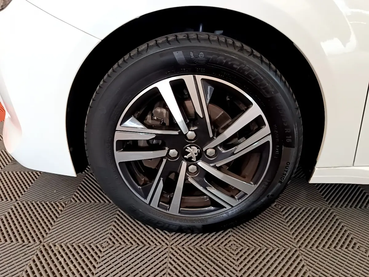 Gros plan sur la roue avant gauche blanche d'une Peugeot 208 PureTech 100 S&S Allure Business avec jante alliage noire et argent.