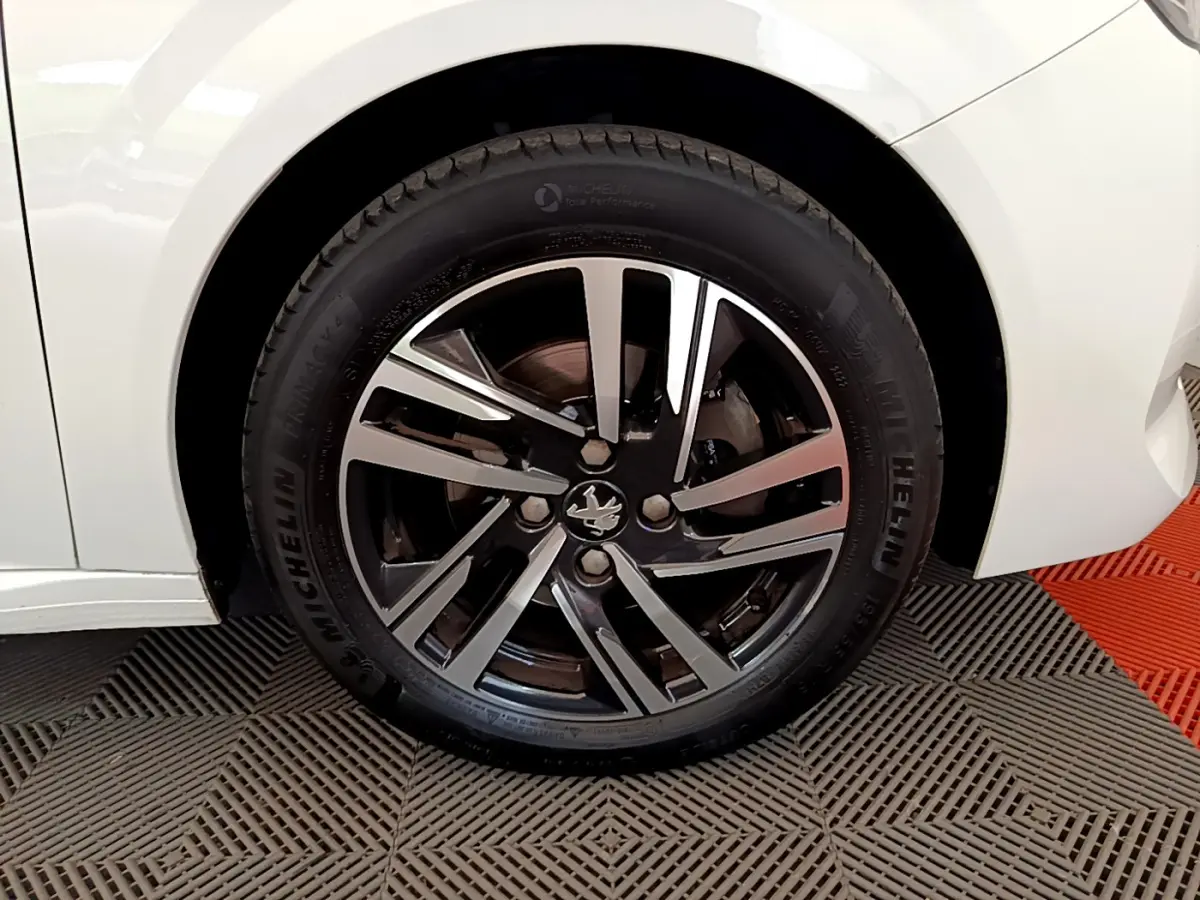 Gros plan sur la roue avant gauche blanche d'une Peugeot 208 2020 avec jante alliage bicolore et logo lion central.