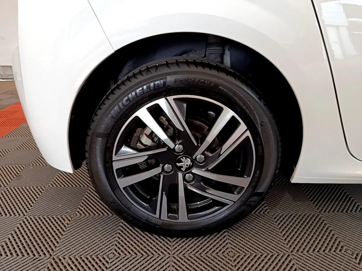 Gros plan sur la roue avant droite d'une Peugeot 208 blanche avec jante alliage noire et argentée.