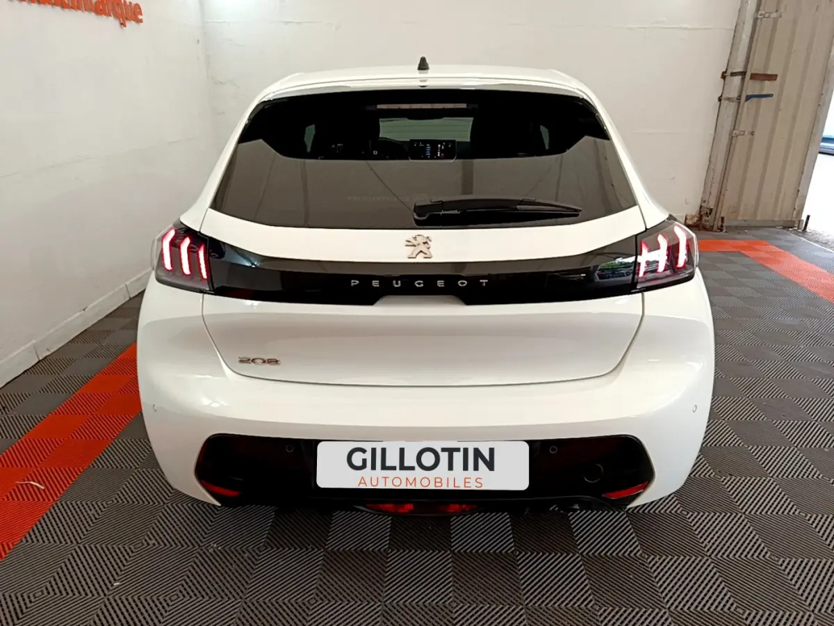 Vue arrière d'une Peugeot 208 blanche avec feux arrière LED distinctifs et logo Peugeot central sur bande noire.