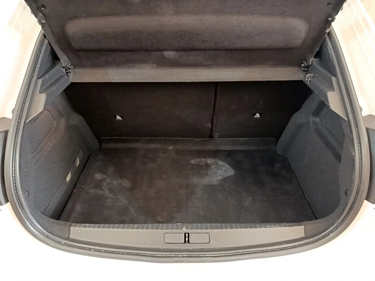 Coffre ouvert vu de l'arrière d'une Peugeot 208 blanche, montrant l'espace de chargement vide et la garniture noire intérieure.