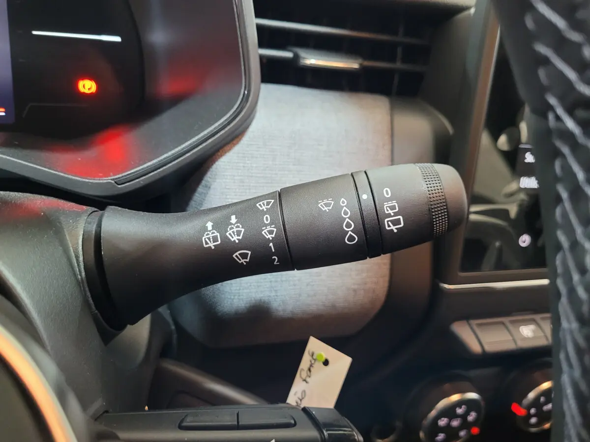 Gros plan sur la commande des essuie-glaces dans l'habitacle gris clair d'une Renault Clio Evolution Blue dCi 2025.