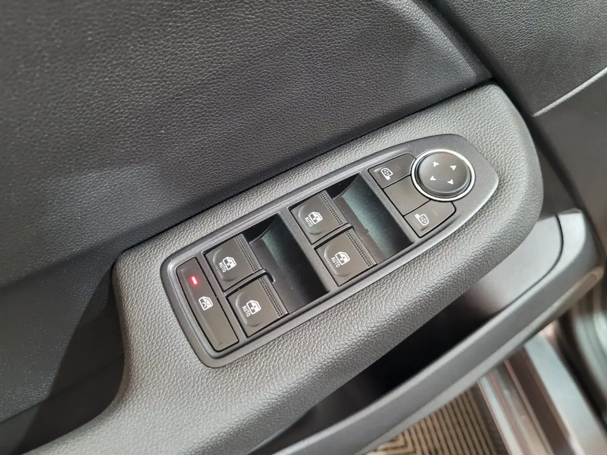 Gros plan sur les commandes des vitres électriques et rétroviseurs sur la portière côté conducteur d'une Renault Clio gris foncé 2025.