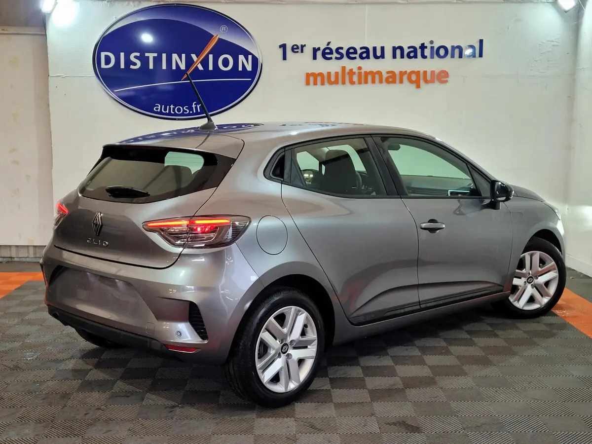 Renault Clio gris foncé vue 3/4 arrière droit avec feux arrière LED allumés dans un showroom.