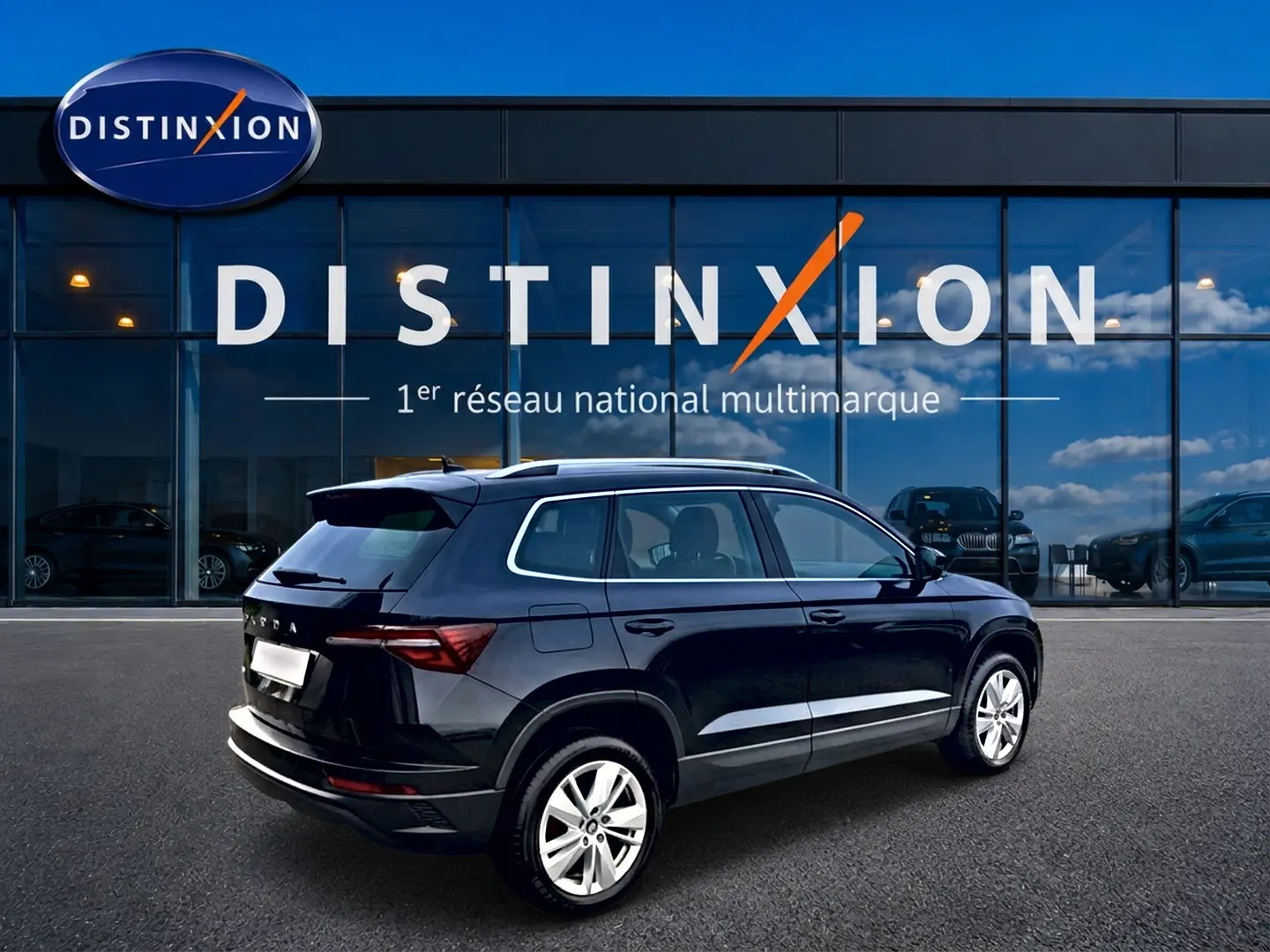 Vue 3/4 arrière droite d'un Skoda Karoq noir 2025 avec jantes alu, barres de toit et becquet arrière visible.