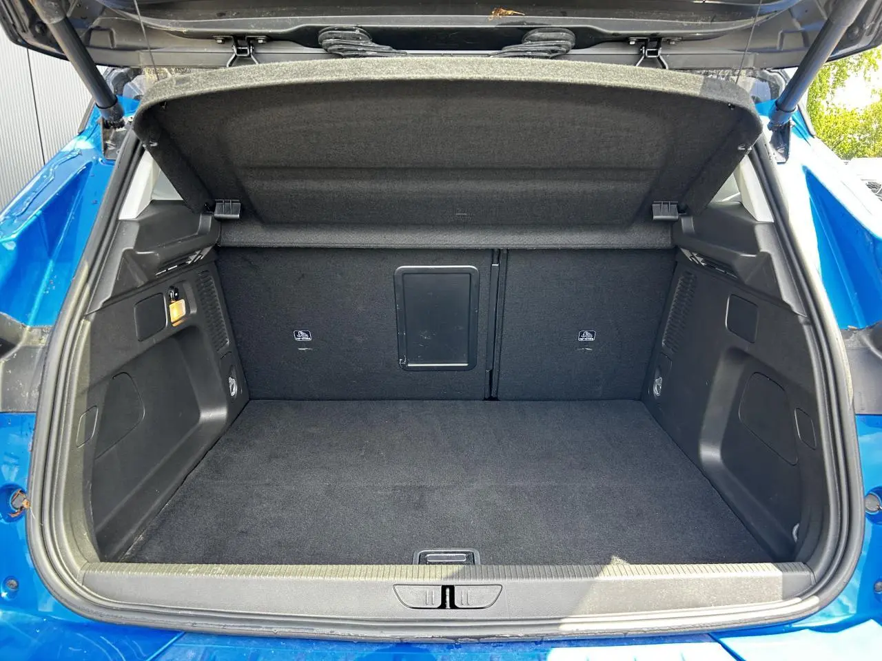 Coffre ouvert vu de l'arrière d'un Opel Grandland bleu Vertigo, espace de chargement vide et tapis noir.