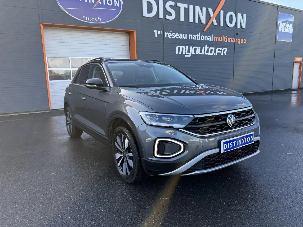 Volkswagen T-Roc gris Indium métallisé en 3/4 avant droit, avec calandre noire et feux LED allumés.