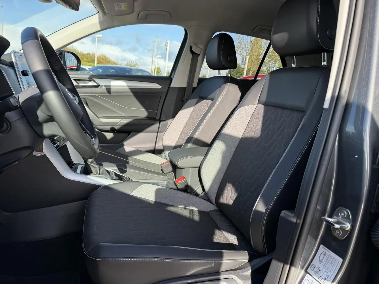 Vue intérieure côté conducteur du Volkswagen T-Roc 2025 gris Indium, sièges tissu et cuir noir avec coutures blanches.