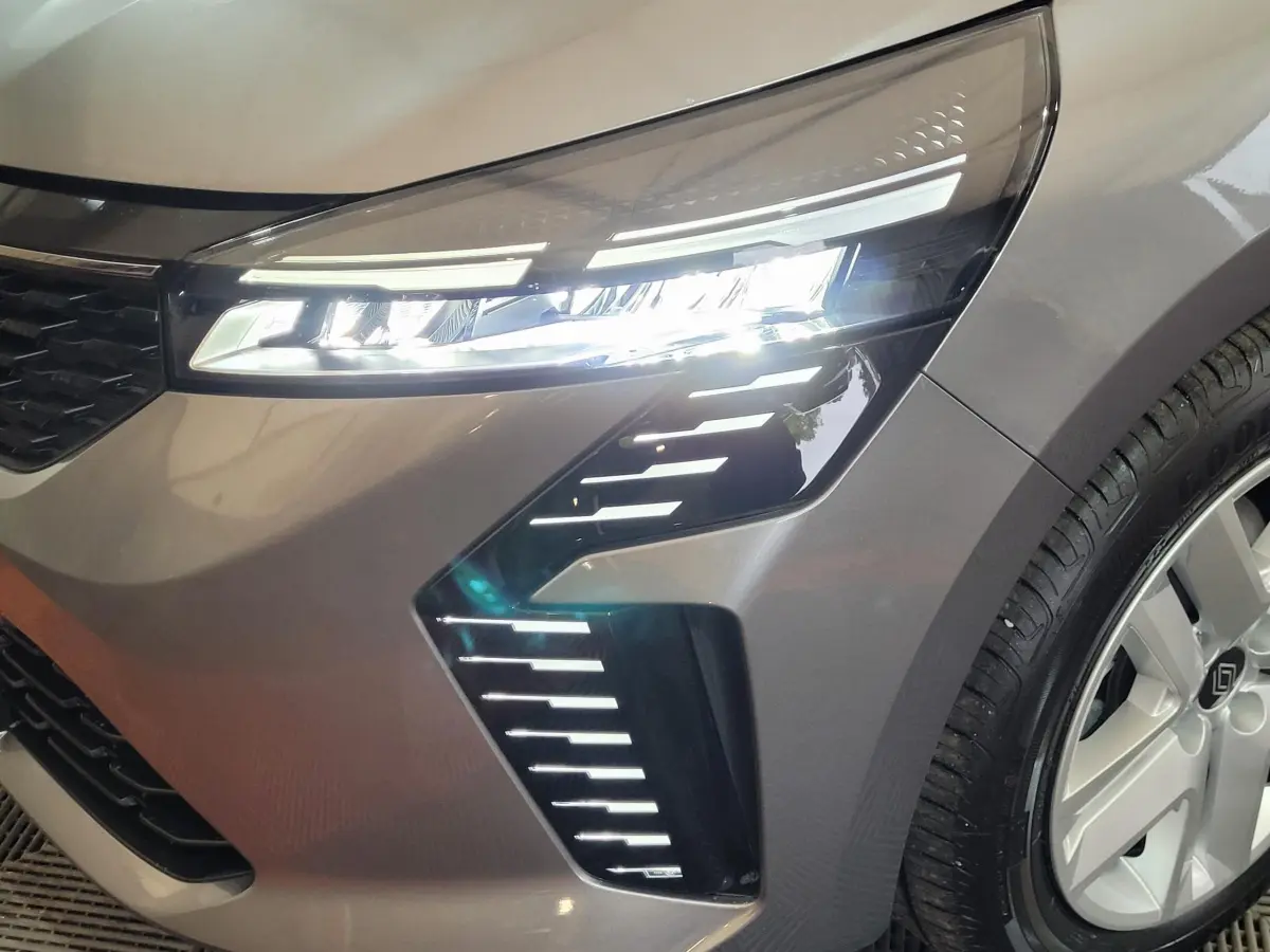 Gros plan sur le phare avant droit allumé d'une Renault Clio gris foncé avec jante alliage visible.