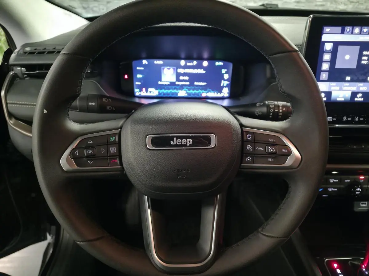 Vue rapprochée du volant noir Jeep Compass 2024 avec commandes intégrées et tableau de bord numérique en arrière-plan.