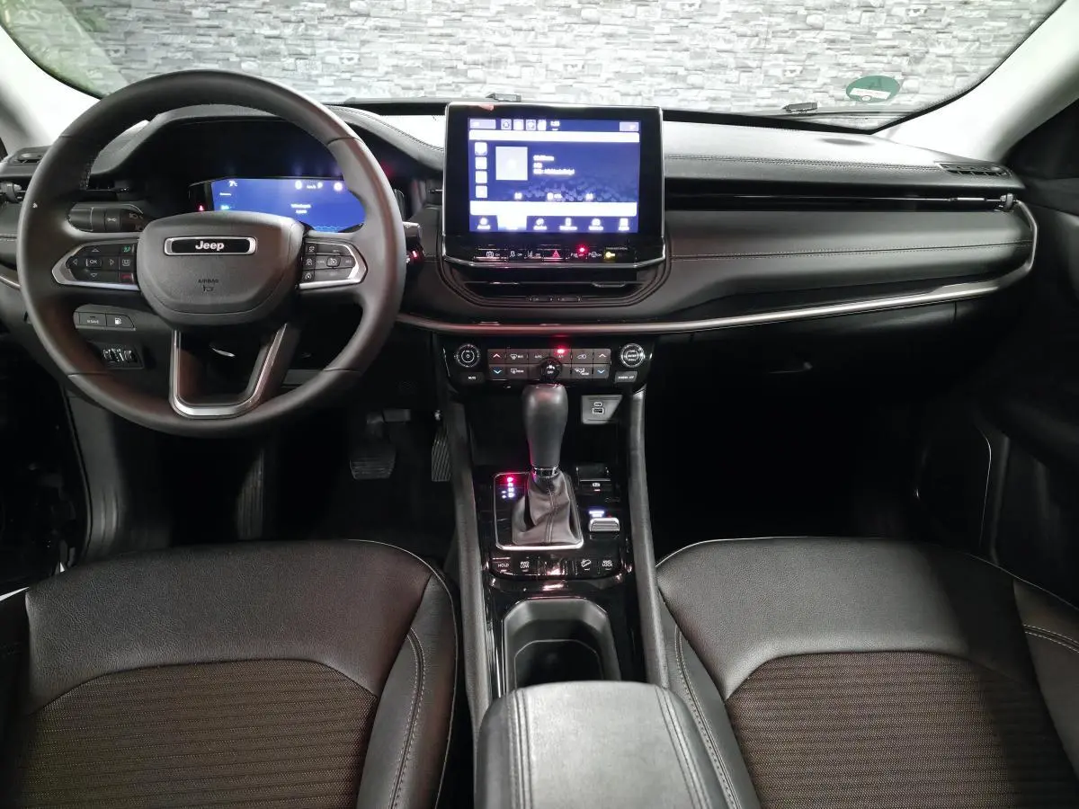 Intérieur noir du Jeep Compass 2024 vu de face, avec tableau de bord numérique et écran tactile central lumineux.