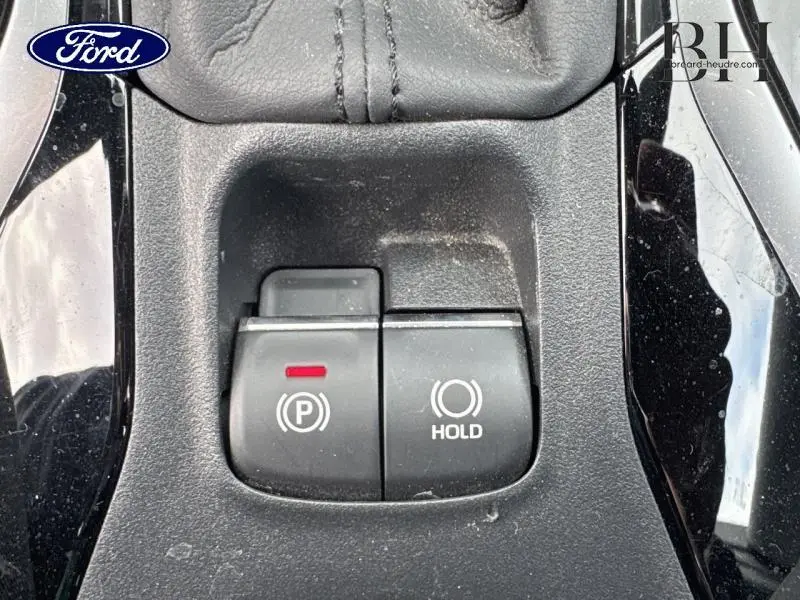 Gros plan sur les commandes électroniques de frein à main et maintien automatique, entourées de plastique noir brillant.