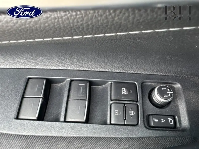 Panneau de commandes des vitres et rétroviseurs côté conducteur en plastique noir avec surpiqûres blanches, intérieur d'une Toyota Corolla gris Manhattan.