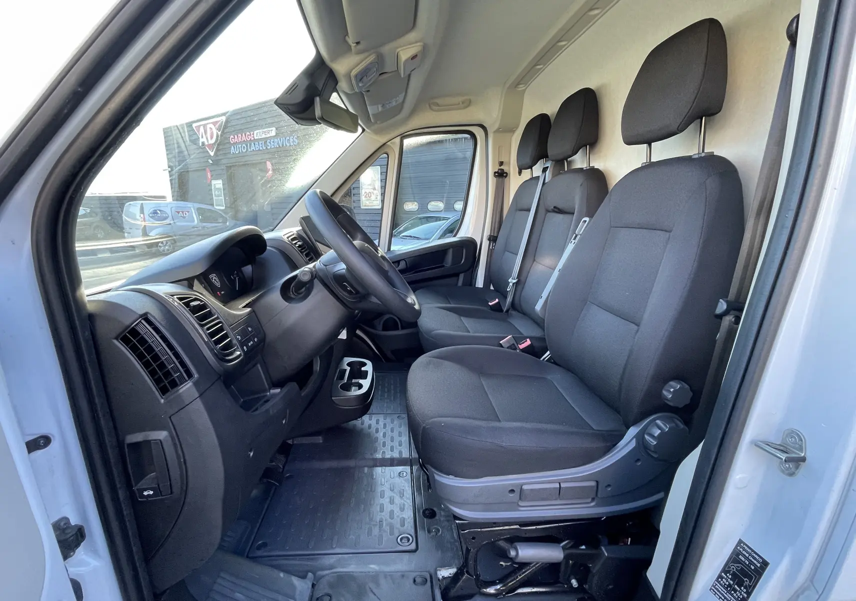Vue intérieure côté conducteur du Peugeot Boxer Fourgon blanc 2025, montrant les trois sièges noirs et le tableau de bord.