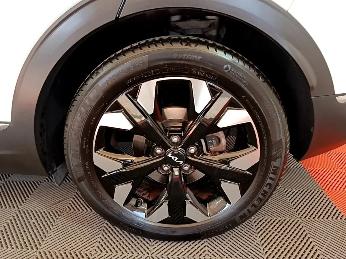 Gros plan sur la roue avant droite du KIA SPORTAGE blanc, avec jante noire et argentée au design moderne.