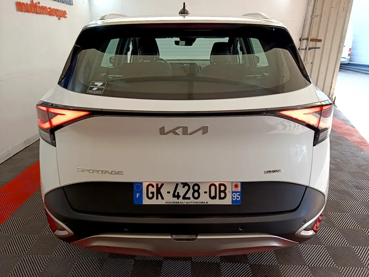 Vue arrière d'un KIA Sportage blanc hybride rechargeable avec feux LED allumés et plaque d'immatriculation française.