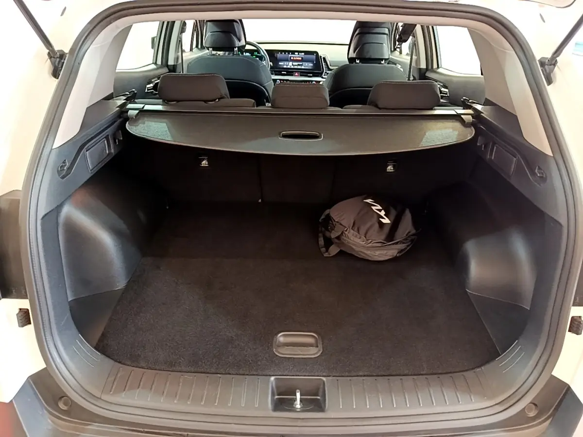 Vue arrière du coffre ouvert du KIA SPORTAGE blanc, avec cache-bagages et sac noir marqué KIA visible à l'intérieur.