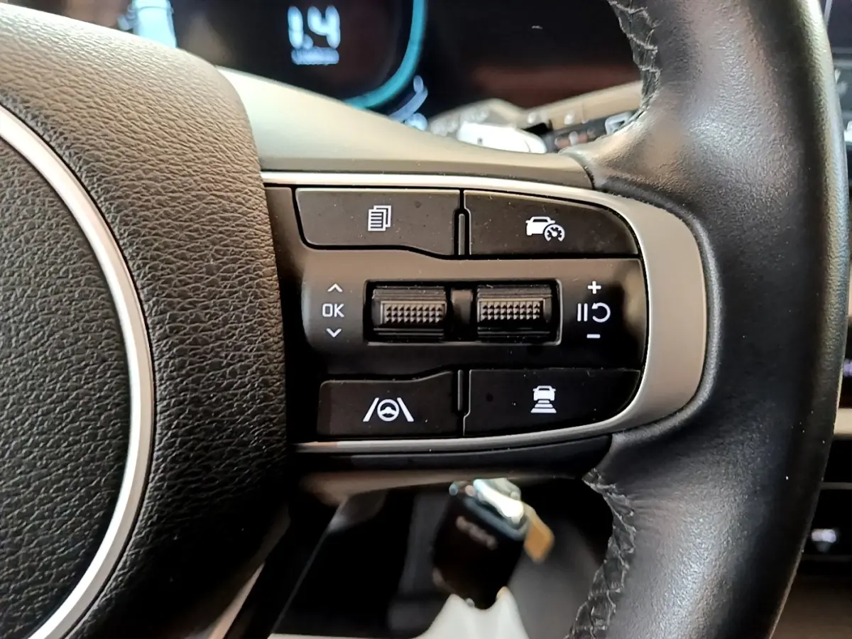 Gros plan sur les commandes multifonctions noires du volant en cuir noir du Kia Sportage blanc, version hybride rechargeable.