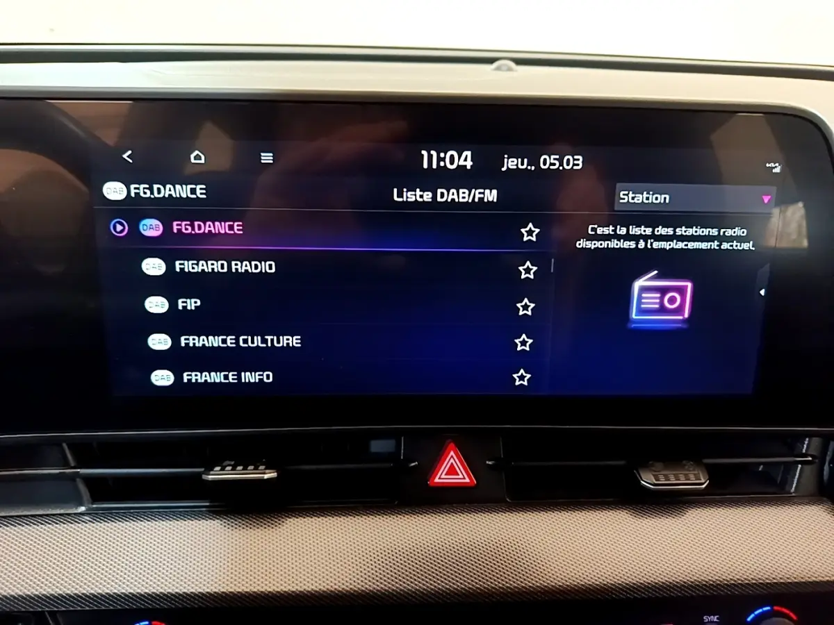 Écran tactile central du tableau de bord du Kia Sportage blanc, affichant la liste des stations radio DAB/FM.