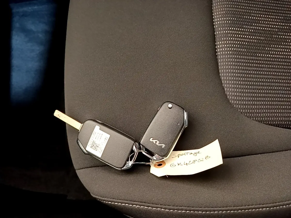 Clé de voiture KIA posée sur un siège tissu noir à l'intérieur d'un KIA SPORTAGE blanc, vue rapprochée.