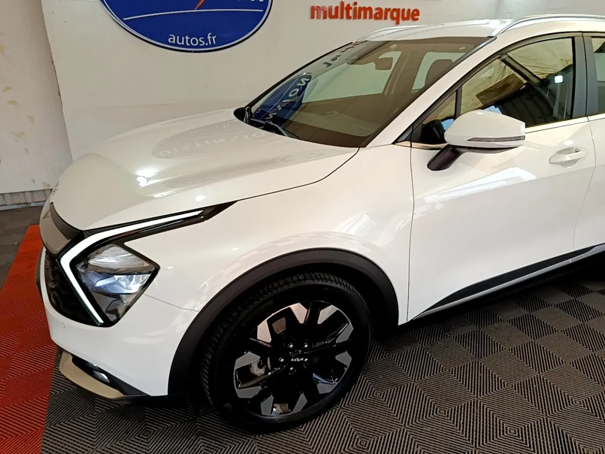 Vue 3/4 avant droit du KIA SPORTAGE blanc avec phares LED en forme de boomerang et jantes noires distinctives.