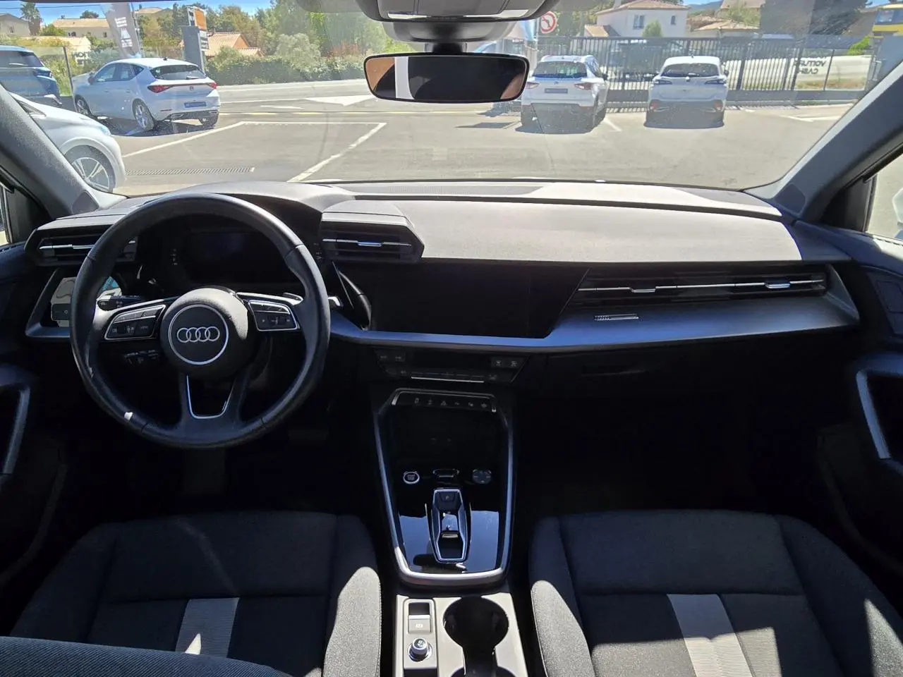 Vue intérieure avant de l'Audi A3 Sportback 2024 avec tableau de bord noir et volant multifonctions cuir.
