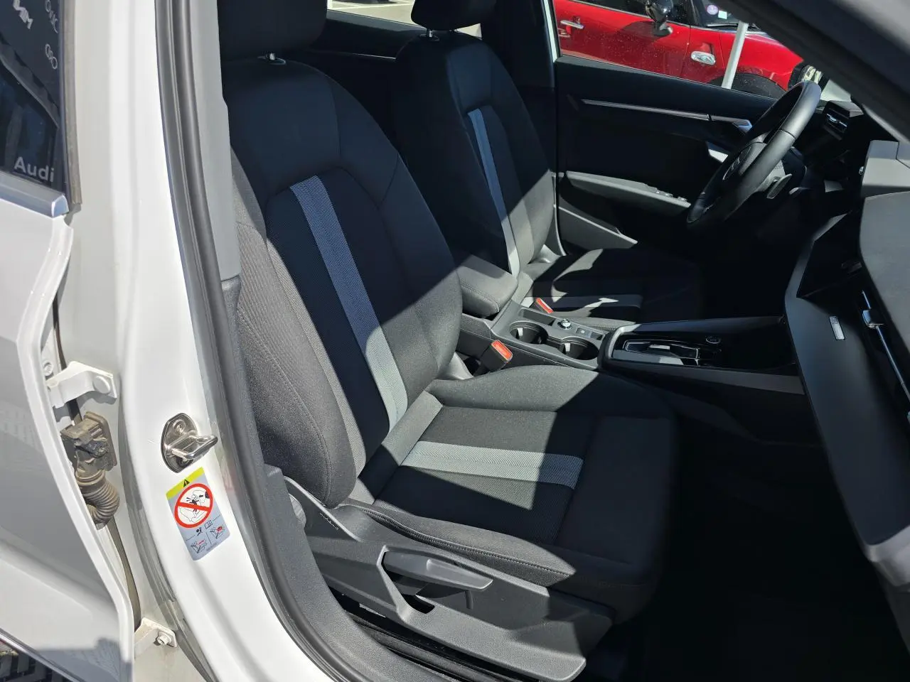 Vue intérieure côté conducteur de l'Audi A3 Sportback 2024 blanc Arkona, sièges tissu noir avec bande grise centrale.