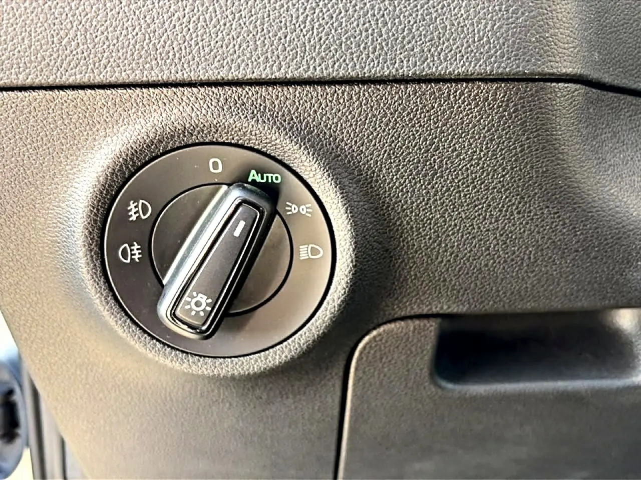 Gros plan sur le bouton de commande des phares du Skoda Karoq 1.5 TSI 150 gris, intérieur noir texturé.