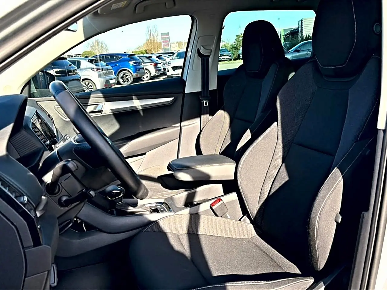 Vue intérieure côté conducteur du Skoda Karoq gris 2025, montrant sièges avant noirs et accoudoir central.