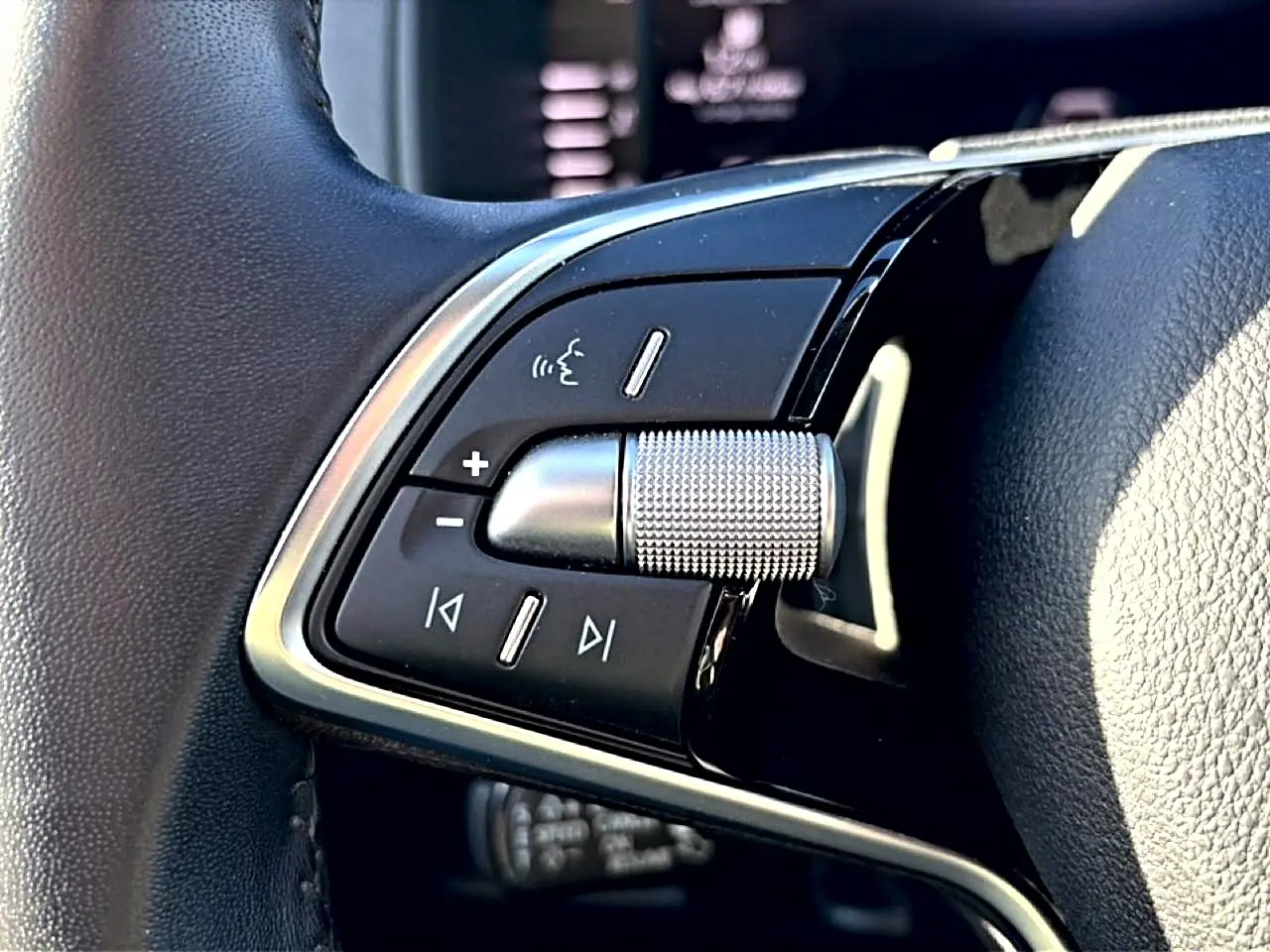 Gros plan sur les commandes audio et vocales sur le côté gauche du volant en cuir noir du Skoda Karoq gris.
