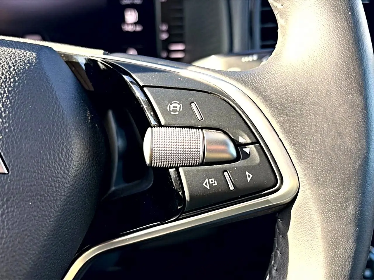 Gros plan sur les commandes noires et argentées du volant cuir du Skoda Karoq gris, côté gauche.