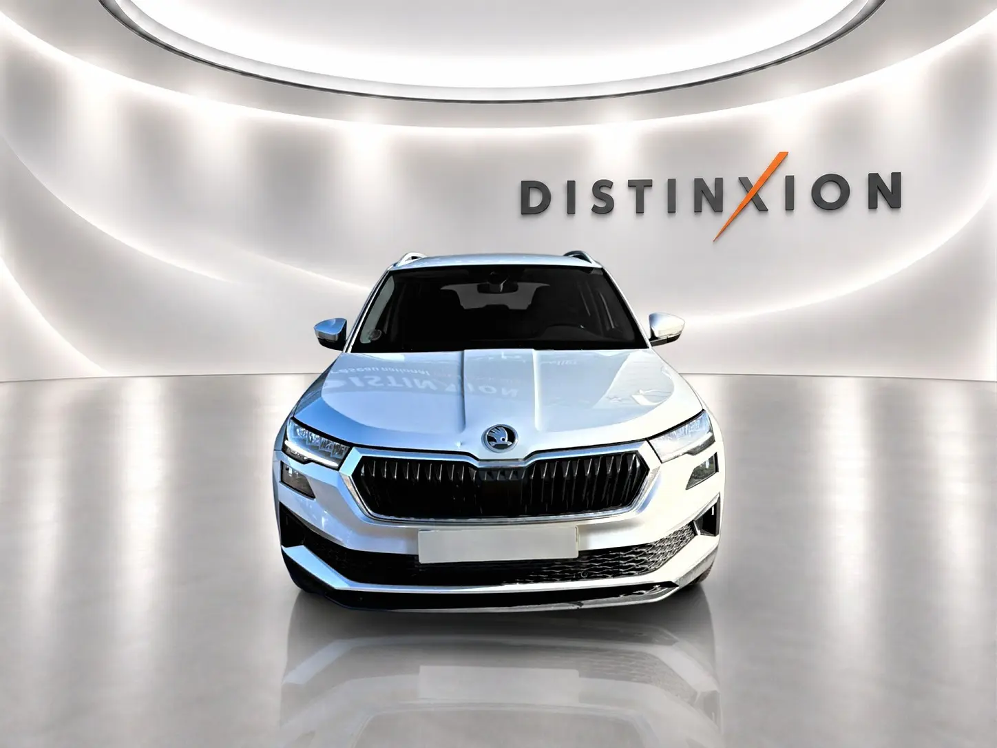 Vue frontale d'un Skoda Karoq gris 2025 avec calandre noire et signature lumineuse LED, dans un showroom épuré.