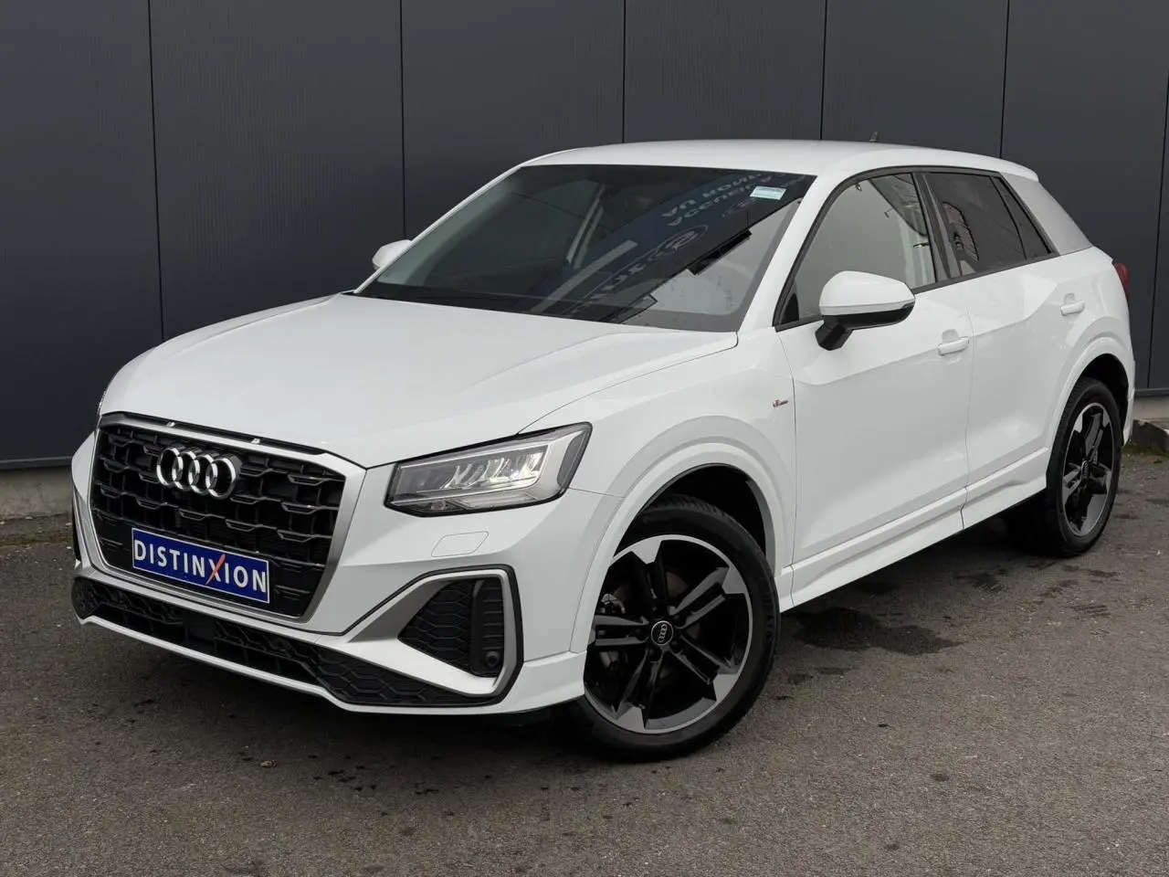 Audi Q2 30 TFSI S-Line blanc Glacier vue 3/4 avant, avec jantes alliage noir poli et calandre noire distinctive.