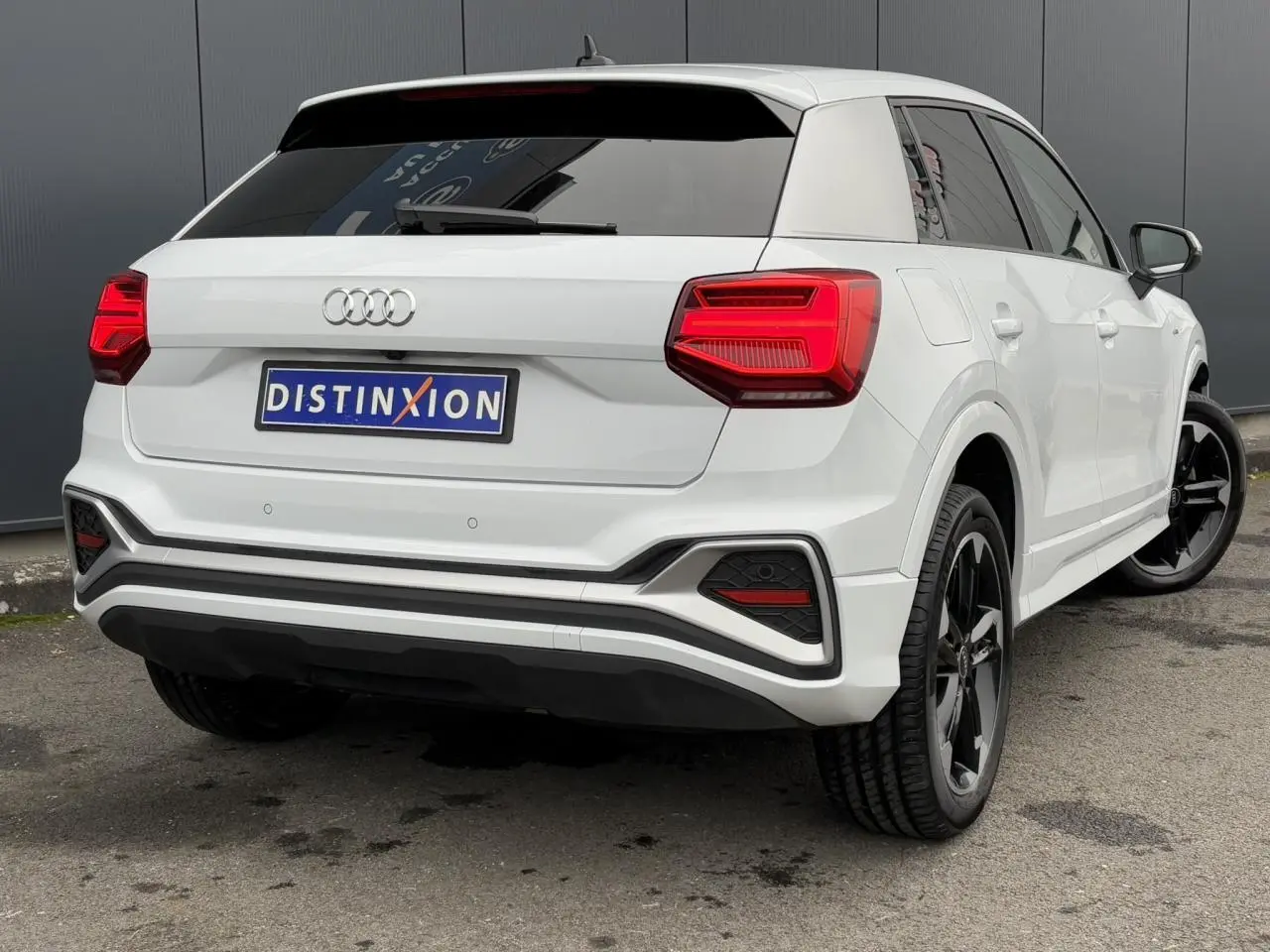 Audi Q2 30 TFSI S-Line blanc Glacier vue 3/4 arrière droit avec jantes noires et feux arrière LED distinctifs.