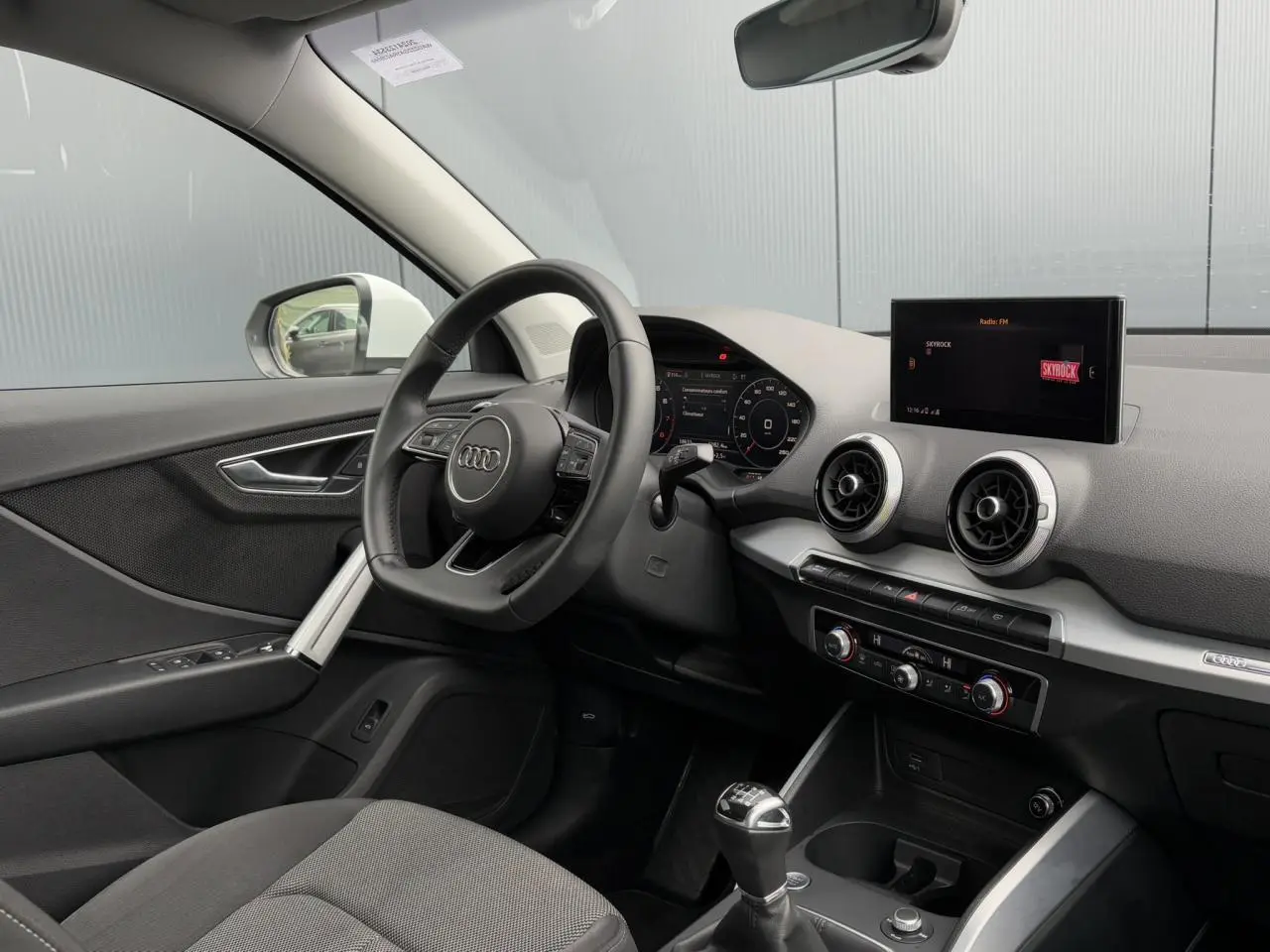 Vue intérieure côté conducteur de l'Audi Q2 30 TFSI S-Line 2024 avec volant cuir, écran central et boîte manuelle.