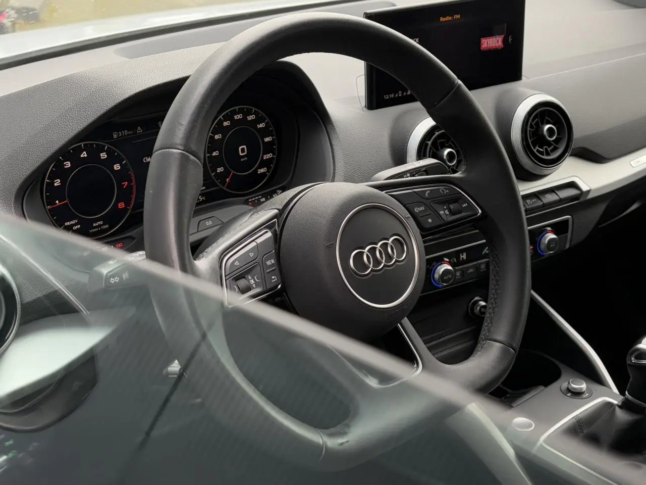 Vue intérieure de l'Audi Q2 30 TFSI S-Line 2024, volant cuir multifonction et tableau de bord digital.