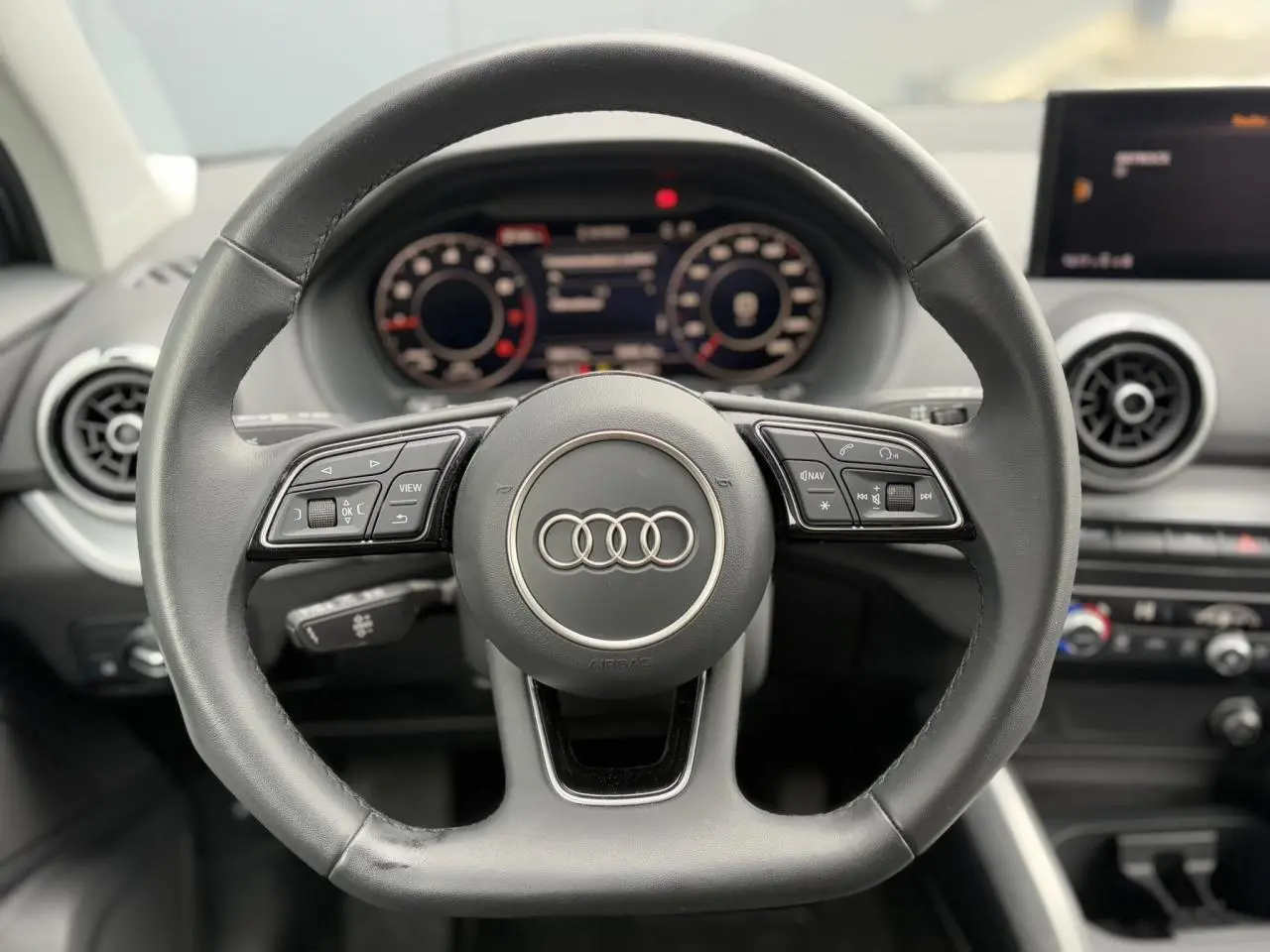 Vue rapprochée du volant multifonction en cuir noir de l'Audi Q2 30 TFSI S-Line avec tableau de bord numérique en arrière-plan.