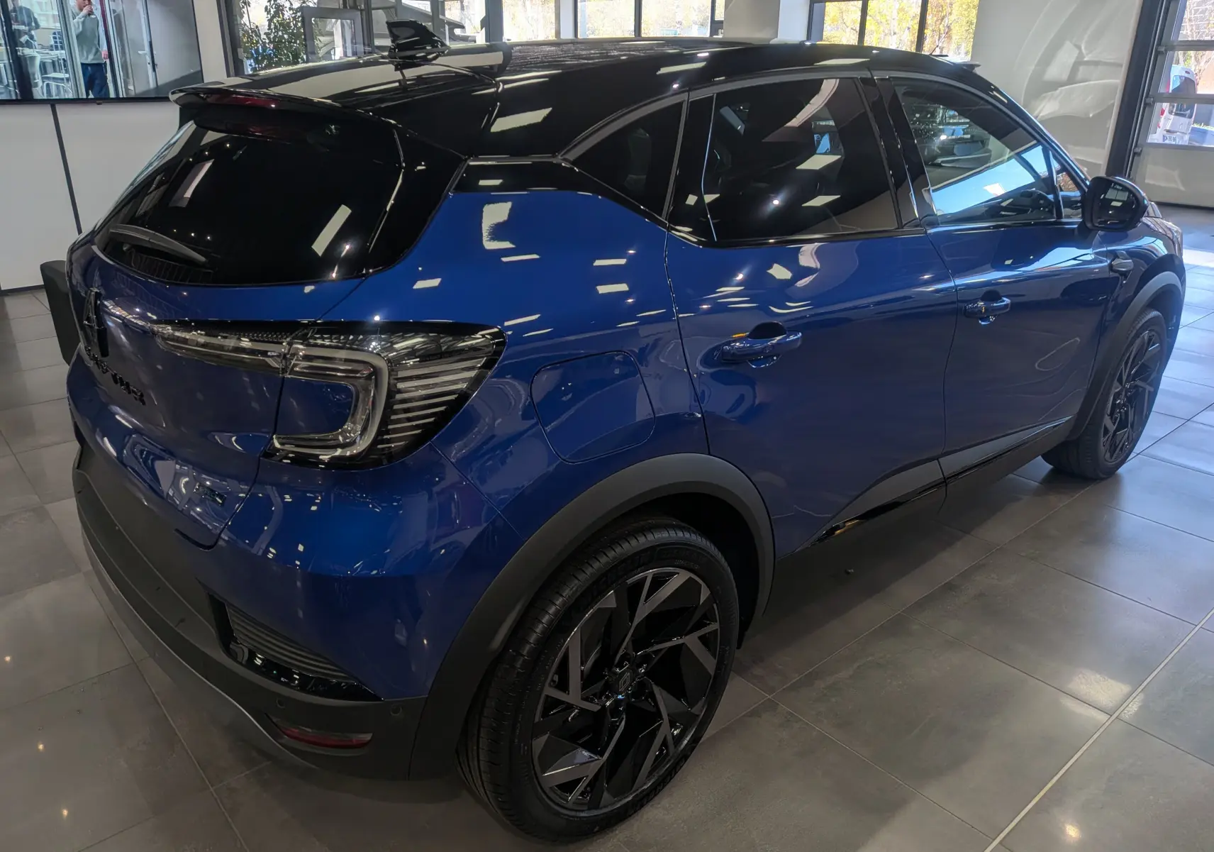 Vue 3/4 arrière droite du Renault Captur E-TECH hybride 2025 en bleu Iron avec toit noir et jantes noires stylées.